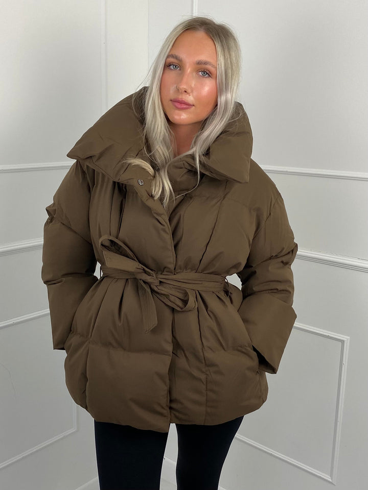 Woman wearing quilted puffer jacket with matching belt outdoors
